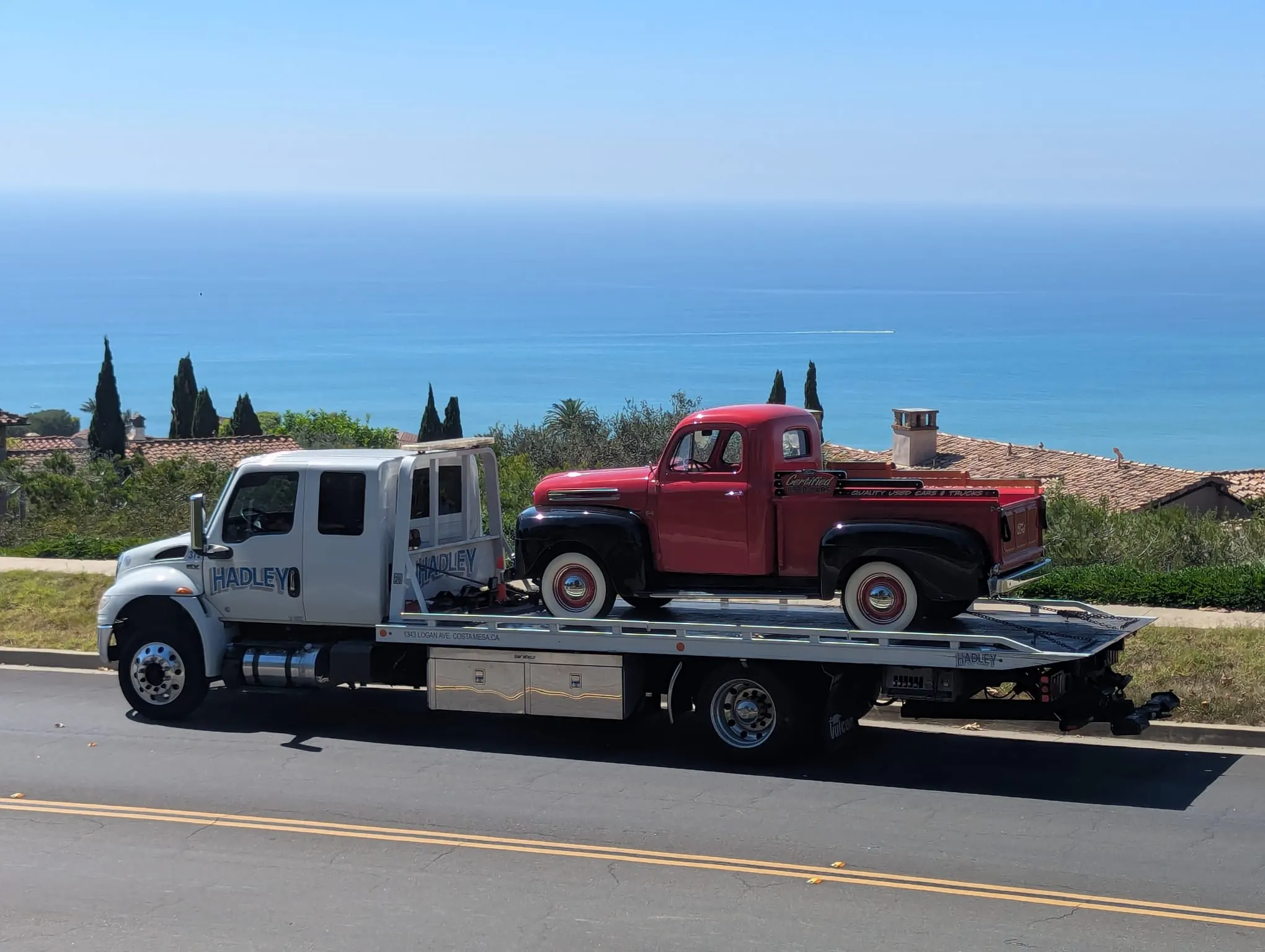 Hadley flatbed carrying a red classic pickup along the Southern California coast