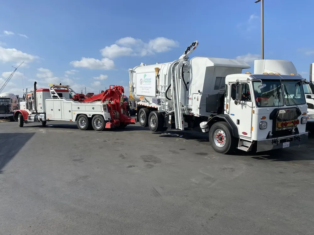 Red and white Hadley wrecker connected to a white refuse truck