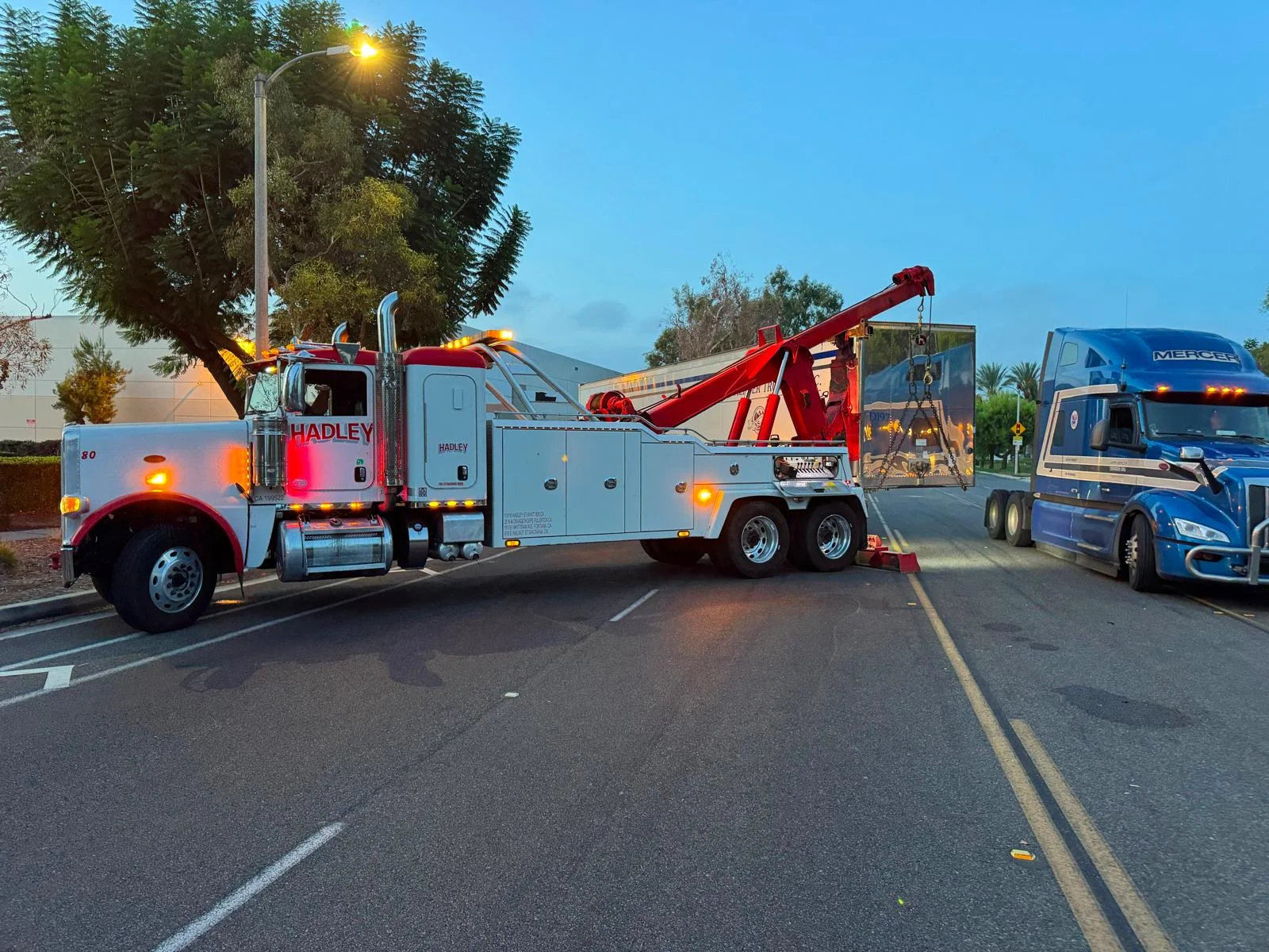 Red and white Hadley heavy recovery truck lifting a semi-trailer