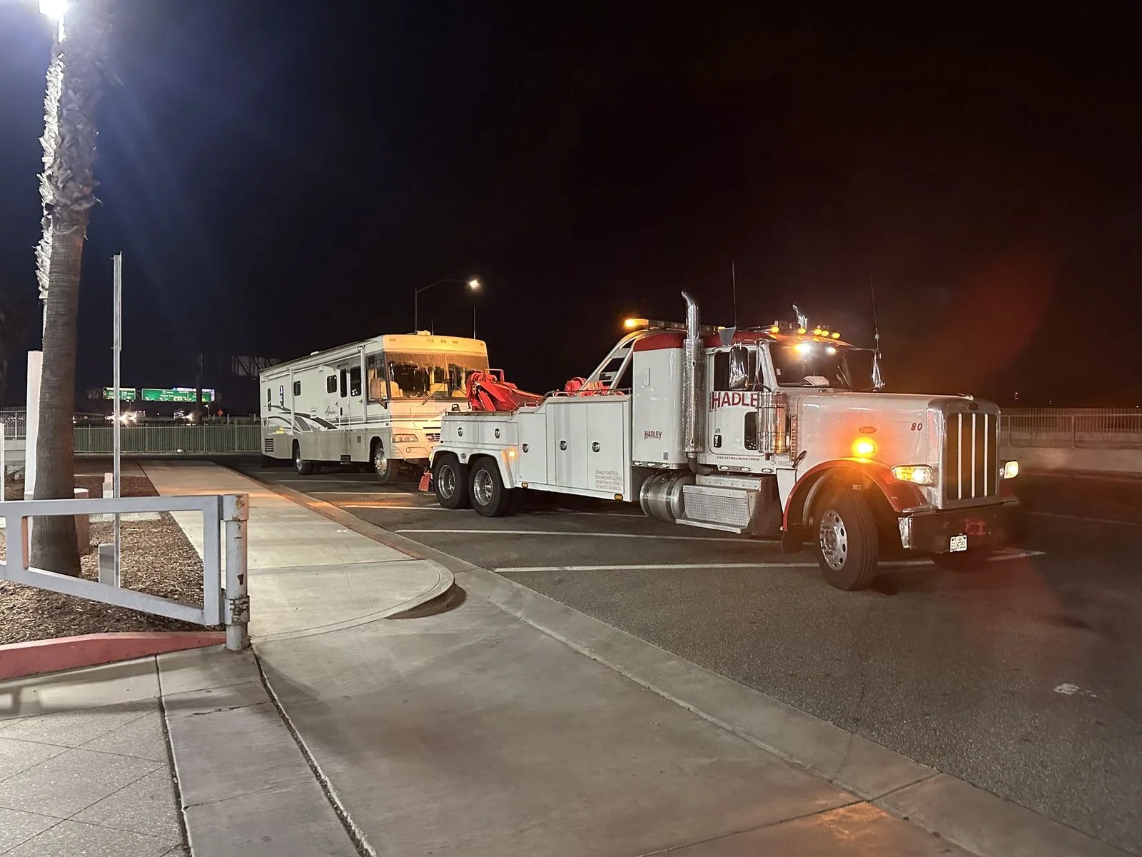 Red and white Hadley wrecker towing a motorhome at night